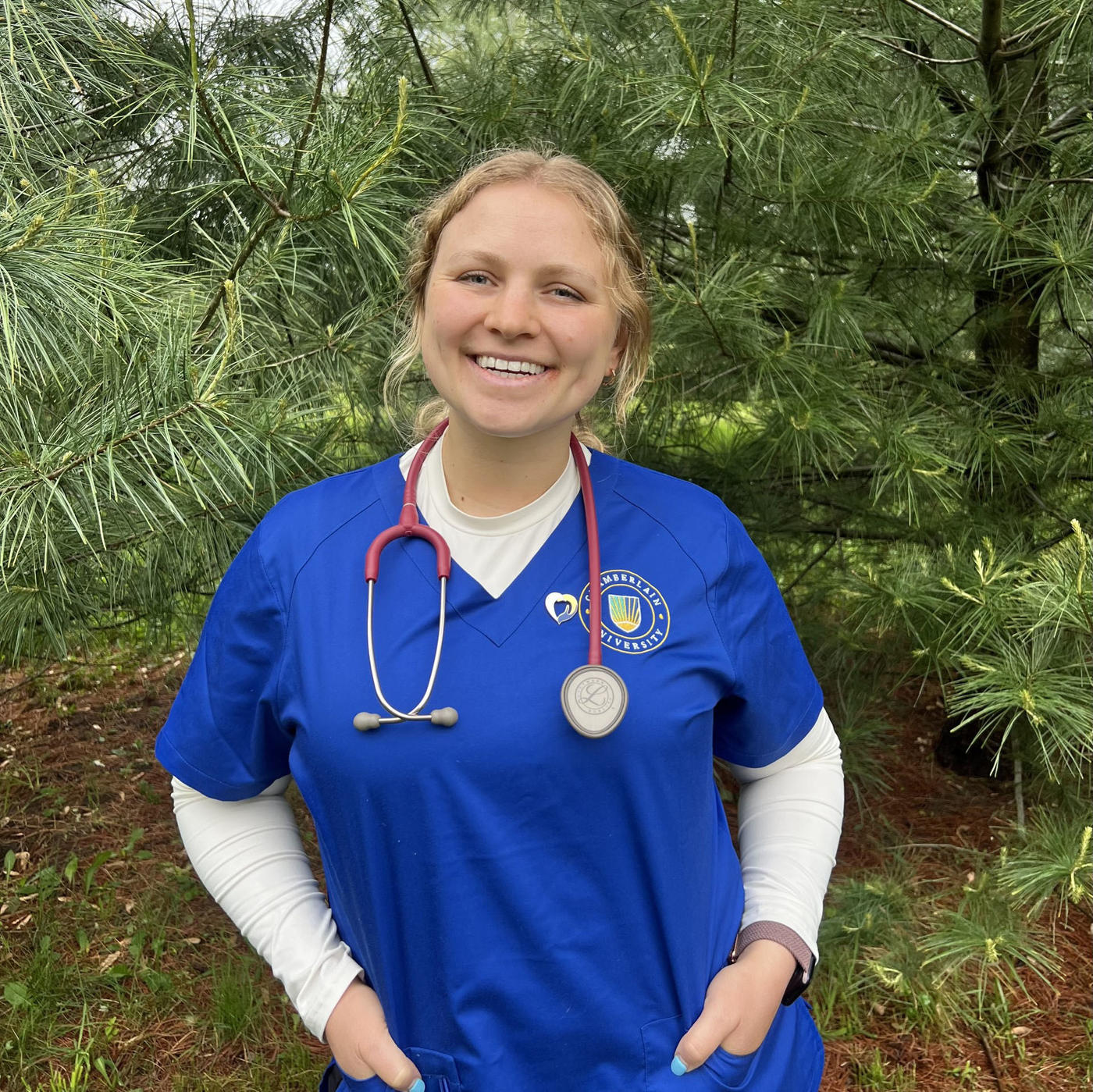Woman in blue scrubs standing in front of tree
